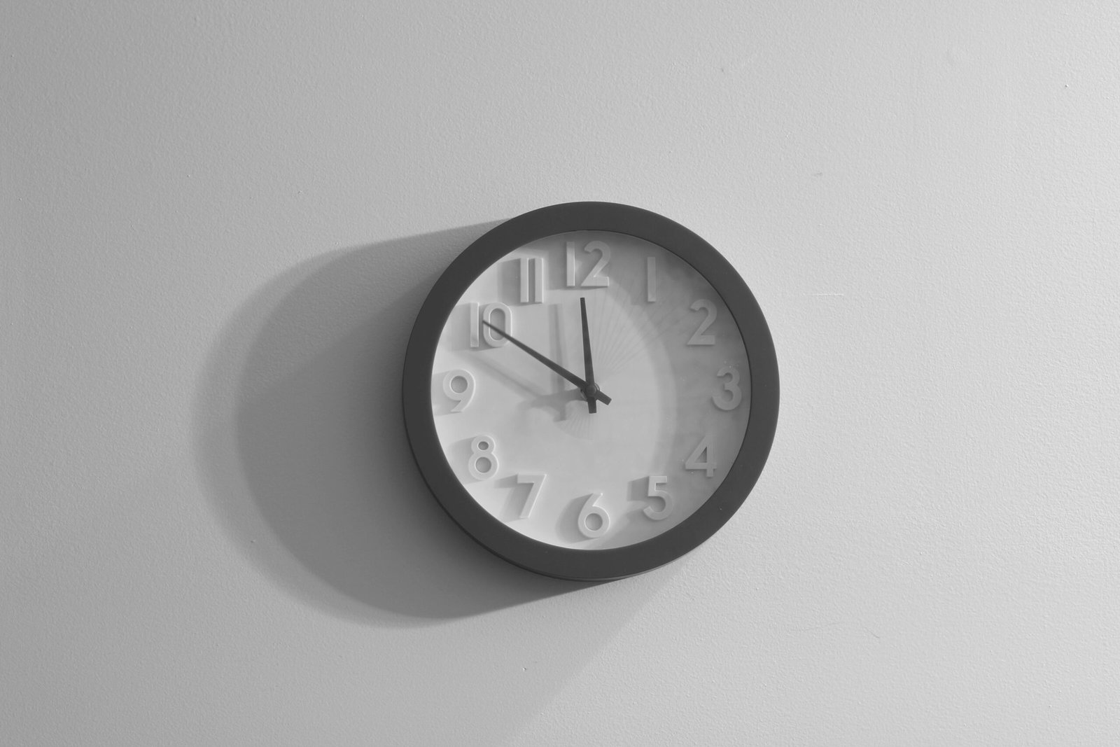 A simple black and white wall clock hangs on a plain wall, showing the time as ten minutes past eleven.