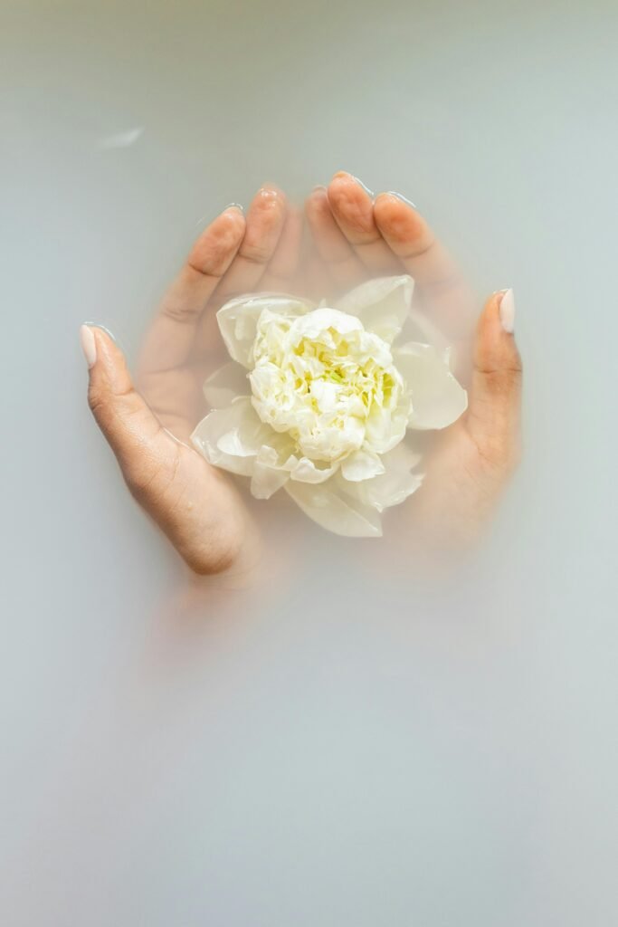 Hands gently hold a white flower, submerged in milky water, creating a serene and peaceful atmosphere.